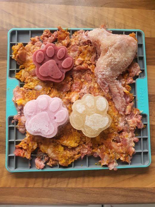 A lick mat loaded with raw minced food, paw-shaped frozen treats and a raw chicken wing